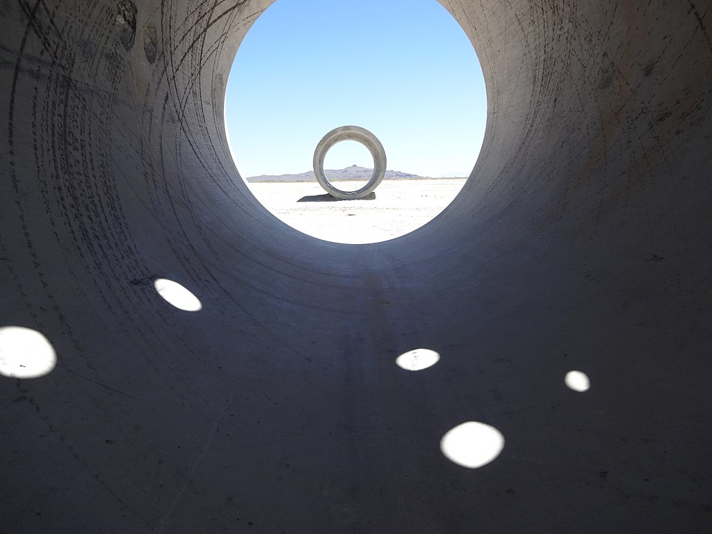 Looking through a massive concrete tube to see a second tube. In the distance, a mountain is visible. 