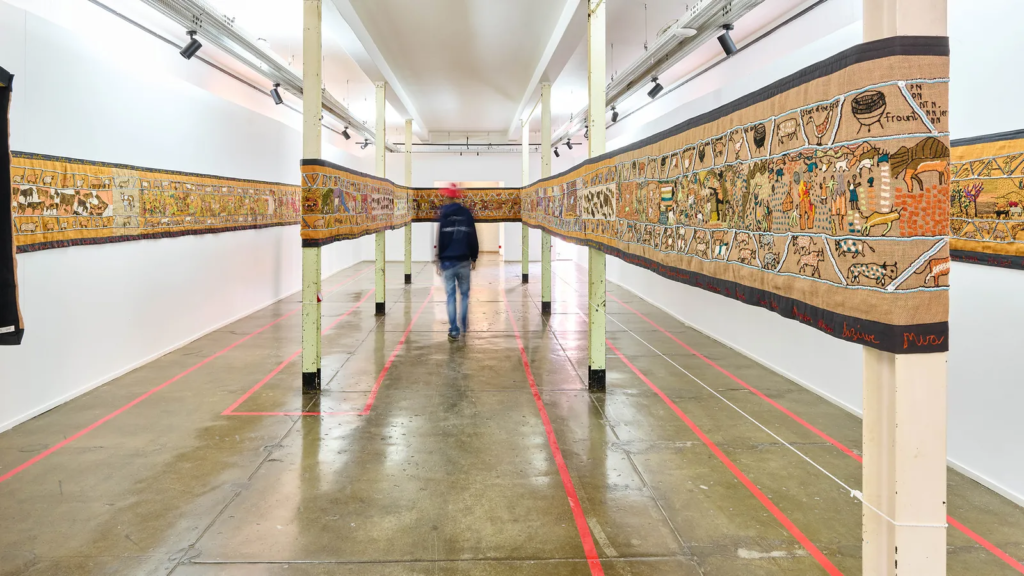 A visitor takes in a tapestry that is stretched between pillars to showcase its entire 120 meter length. 