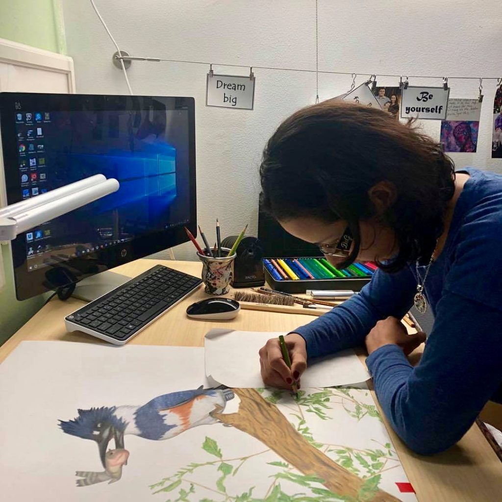 A woman colours an illustration of a kingfisher with a coloured pencil. 