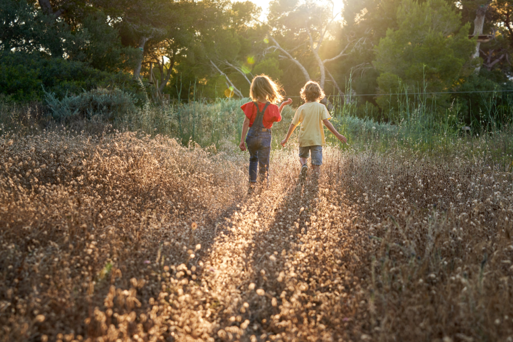 Two children run through a field of flower seedheads. 