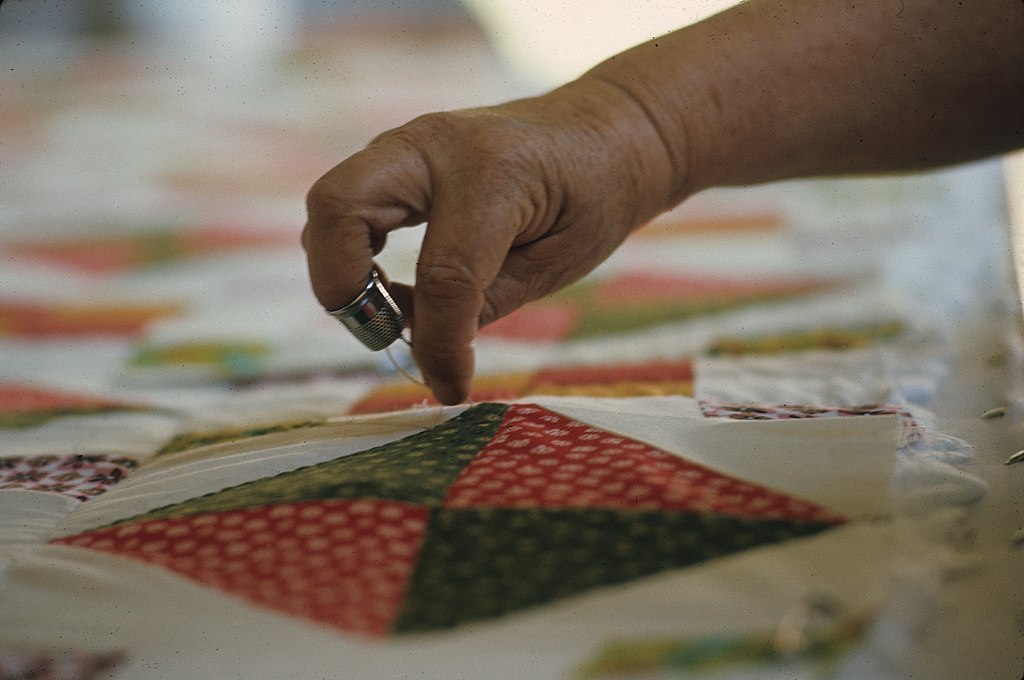 A woman's hand adds stitches to a handmade quilt. 