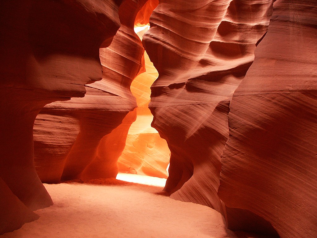 A desert canyon comprised of towering red sandstone cliffs illuminated by sunlight. 