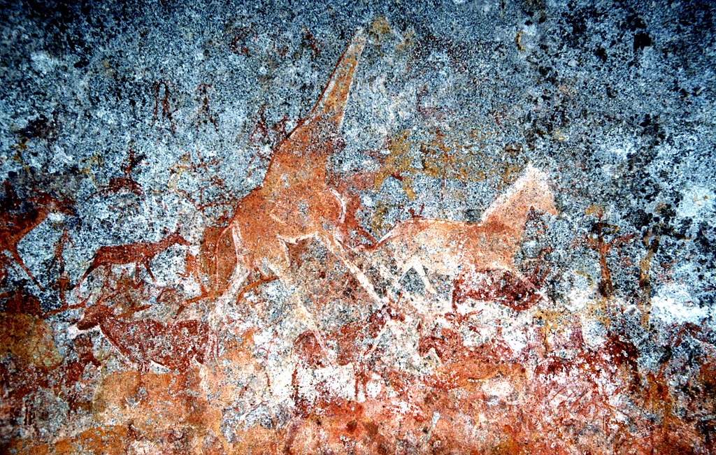Red ochres drawings of animals on a cave wall including giraffes, horses, and antelope. 