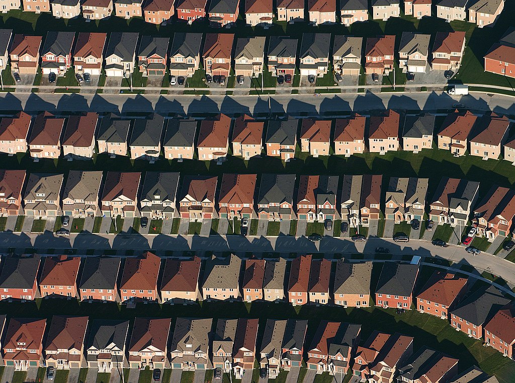 An aerial photograph of a suburb. The houses are neutral shades of brown, grey, and black. 