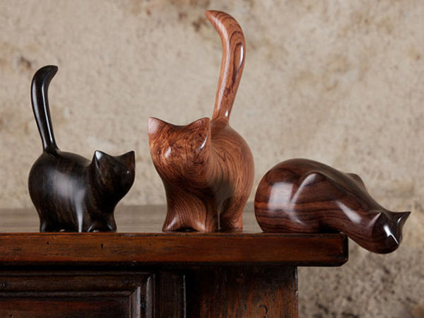 Three wooden carvings of cats sit on the edge of a shelf.